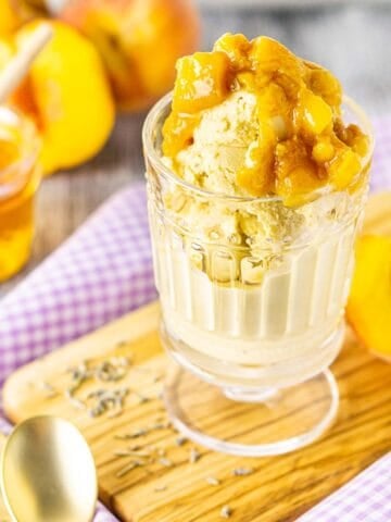 A glass of honey-lavender ice cream on purple clothe with peaches and honey in the background.