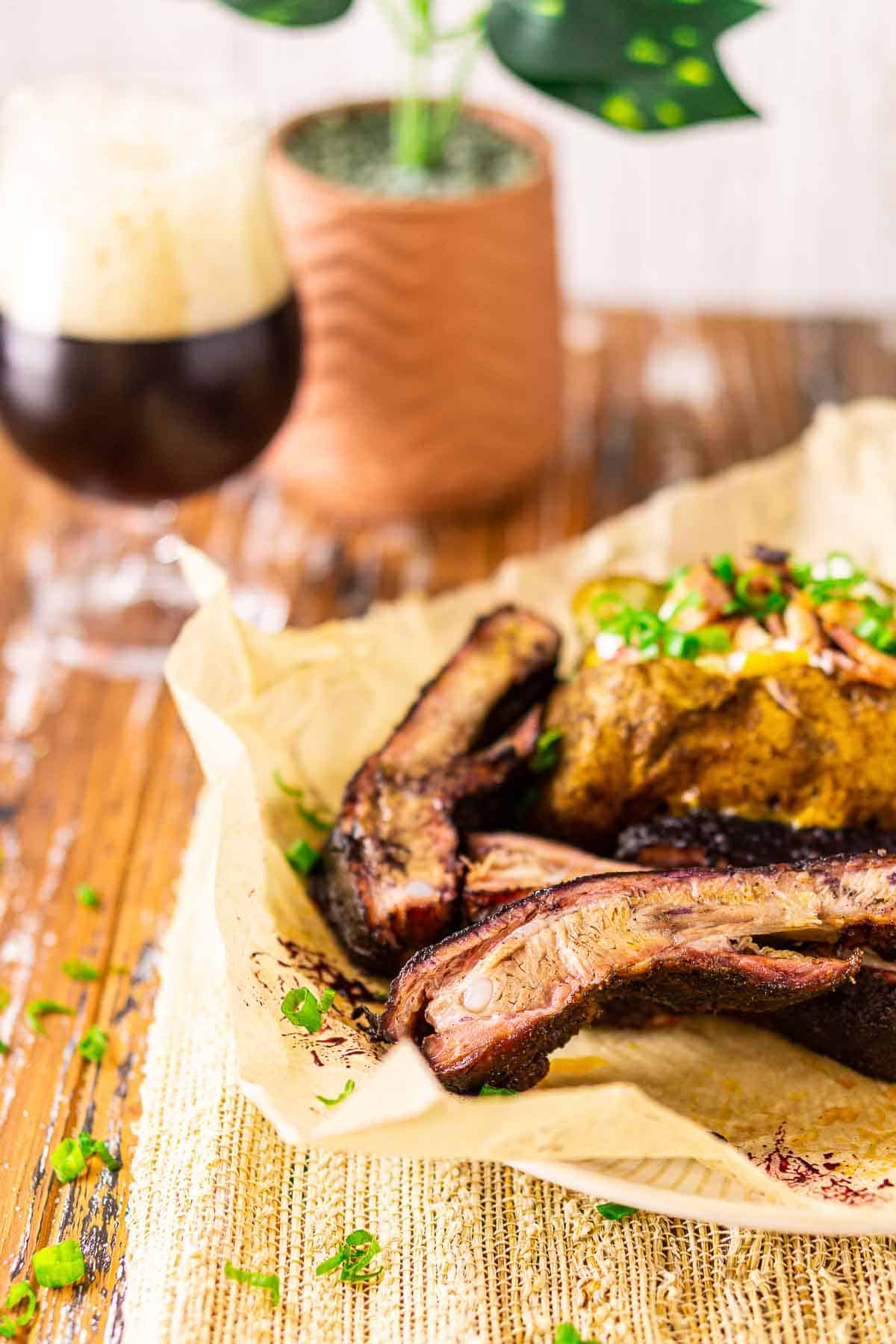 The pellet grill ribs on a white plate with a baked potato behind it and green onions scattered around the food.