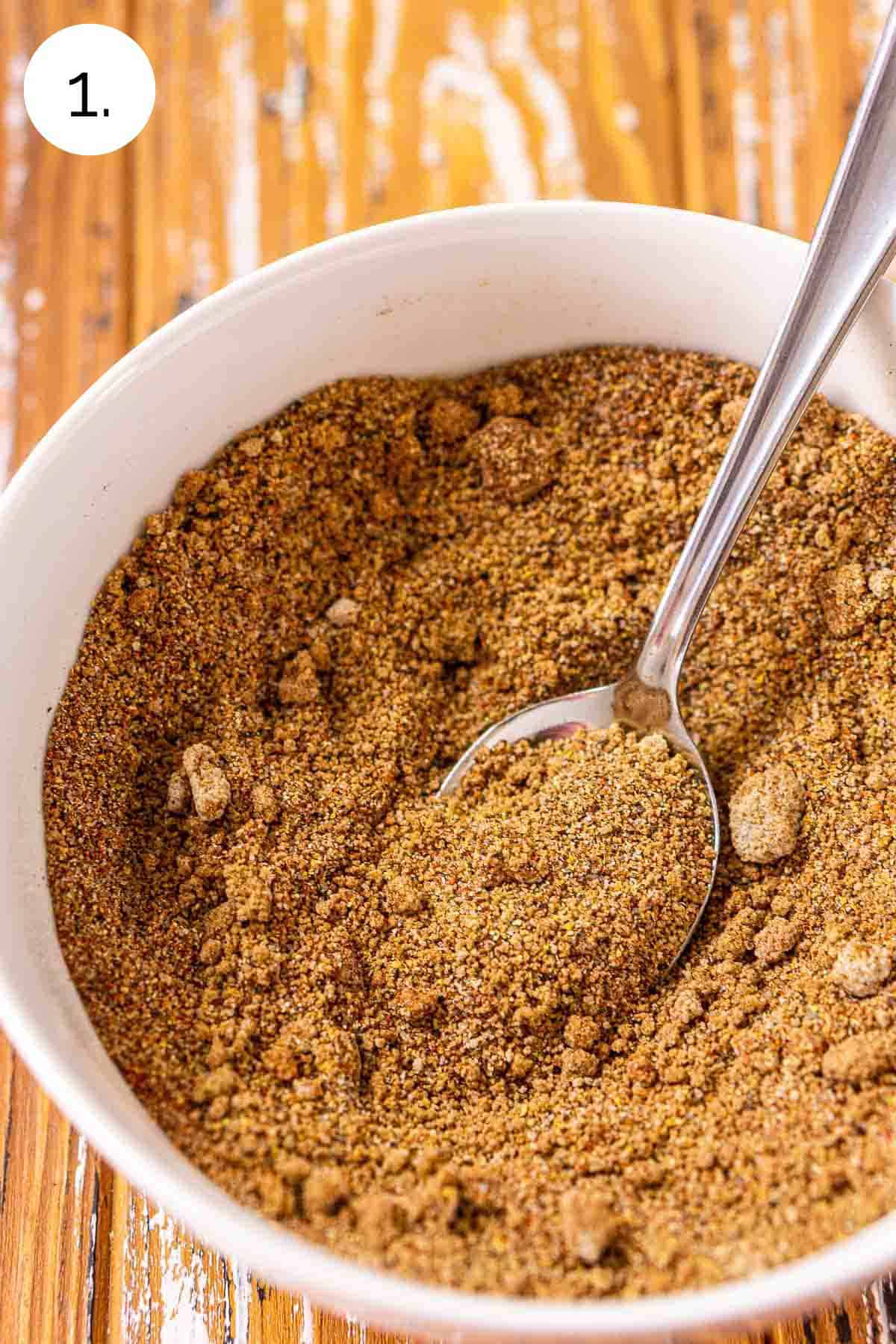 The spice mixture in a white small bowl on a wooden surface after stirring.