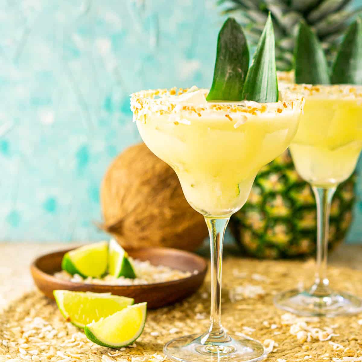 Two pineapple-coconut margaritas on a placemat with a pineapple and coconut in the background.