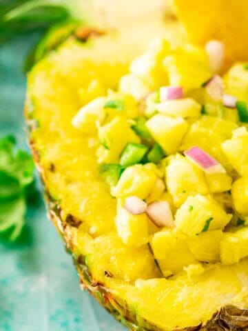 A close-up shot of the pineapple pico de gallo in a pineapple bowl on a blue surface with cilantro around it.