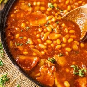 A cast-iron skillet filled with smoked baked beans on burlap with fresh thyme to the side.