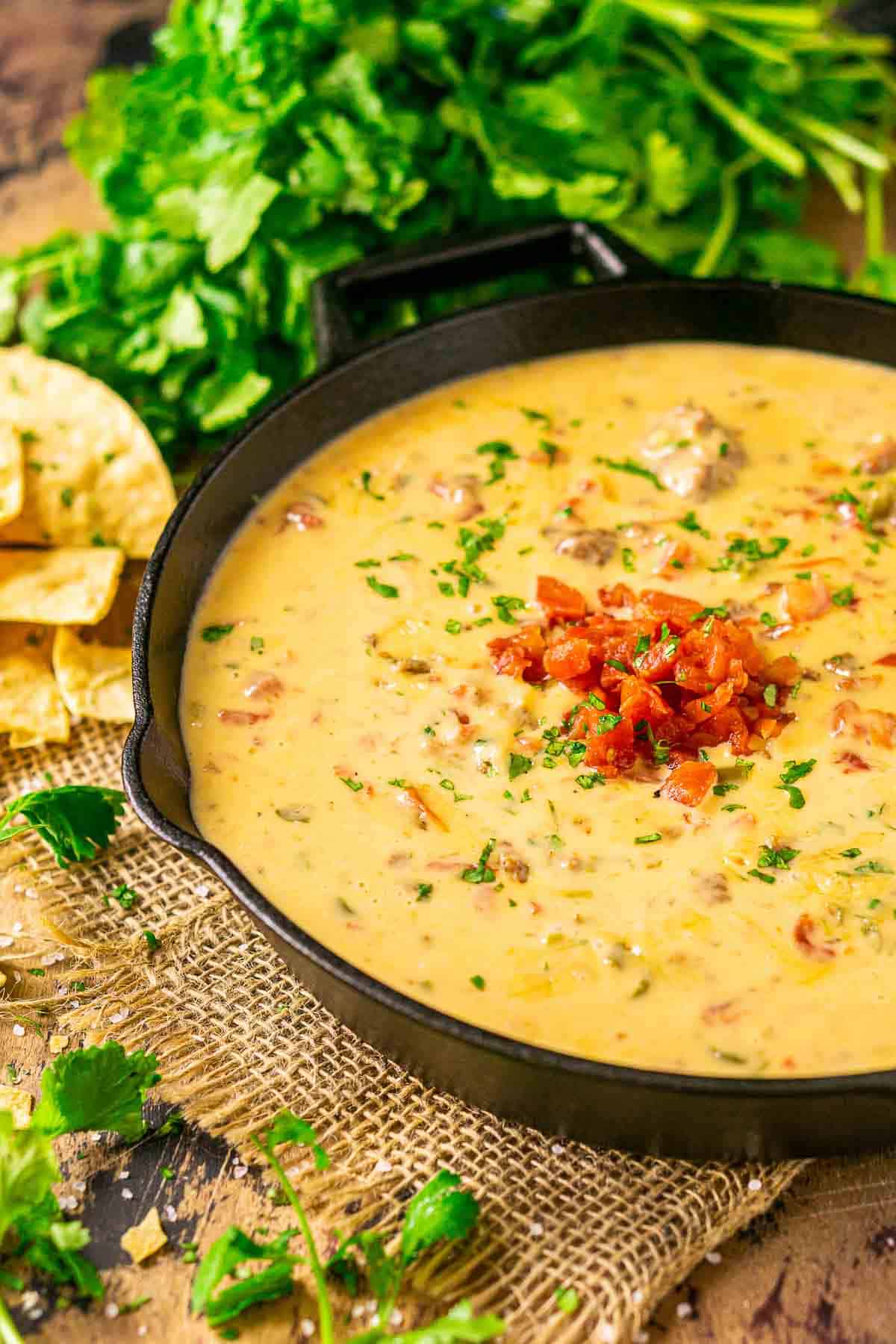 Looking down on a cast-iron skillet full of smoked queso dip on a piece of burlap.