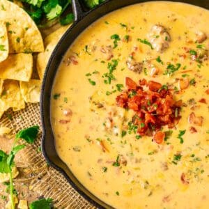 An aerial view of the smoked queso dip on burlap with cilantro and crushed tortilla chips to the left.