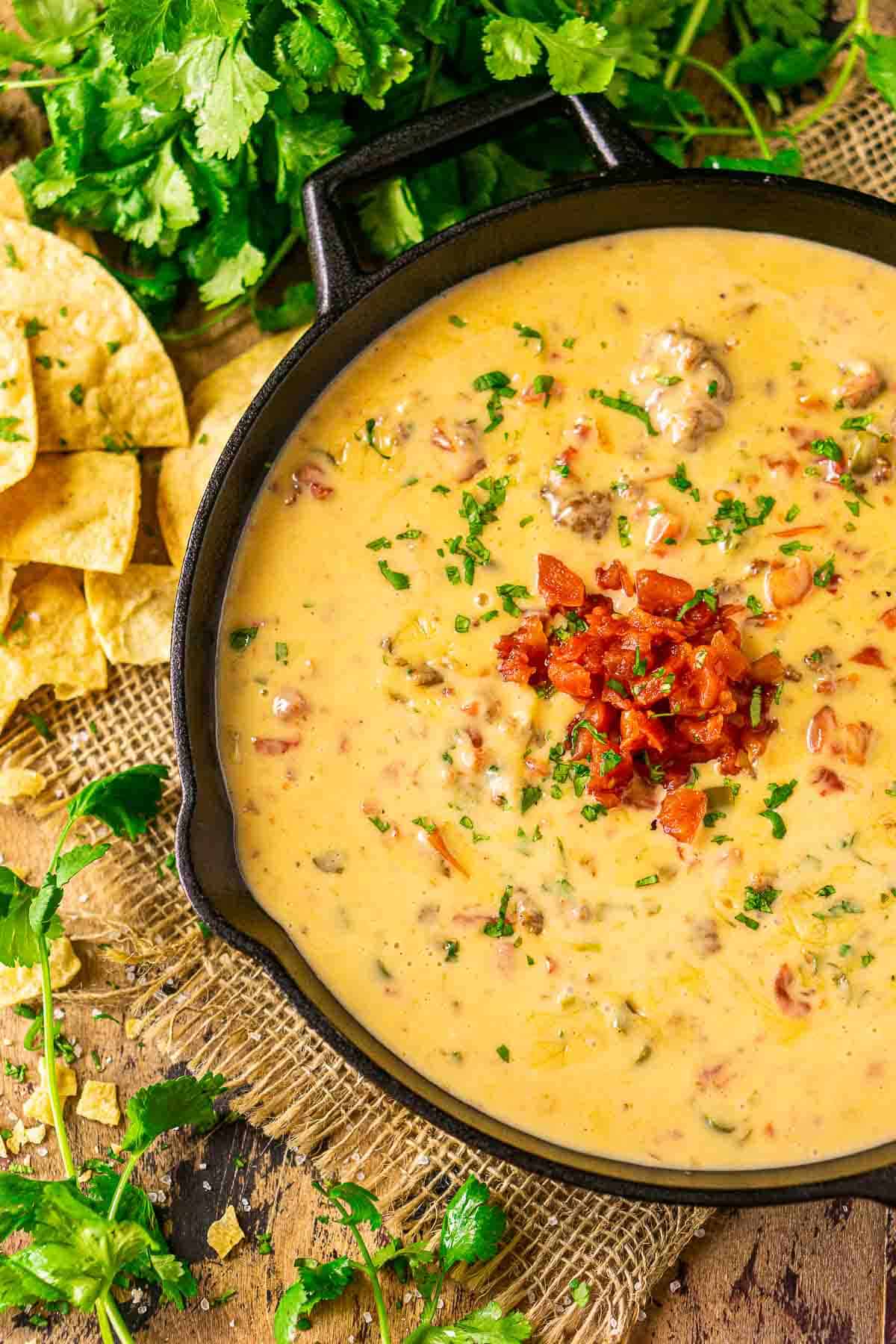 An aerial view of the smoked queso dip on burlap with cilantro and crushed tortilla chips to the left.