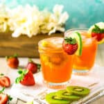 Two strawberry-kiwi margaritas on a white wooden board with slices of kiwi and strawberries around them against a blue background.