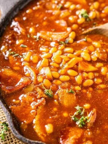 A cast-iron skillet with baked beans on burlap with fresh thyme to the side.