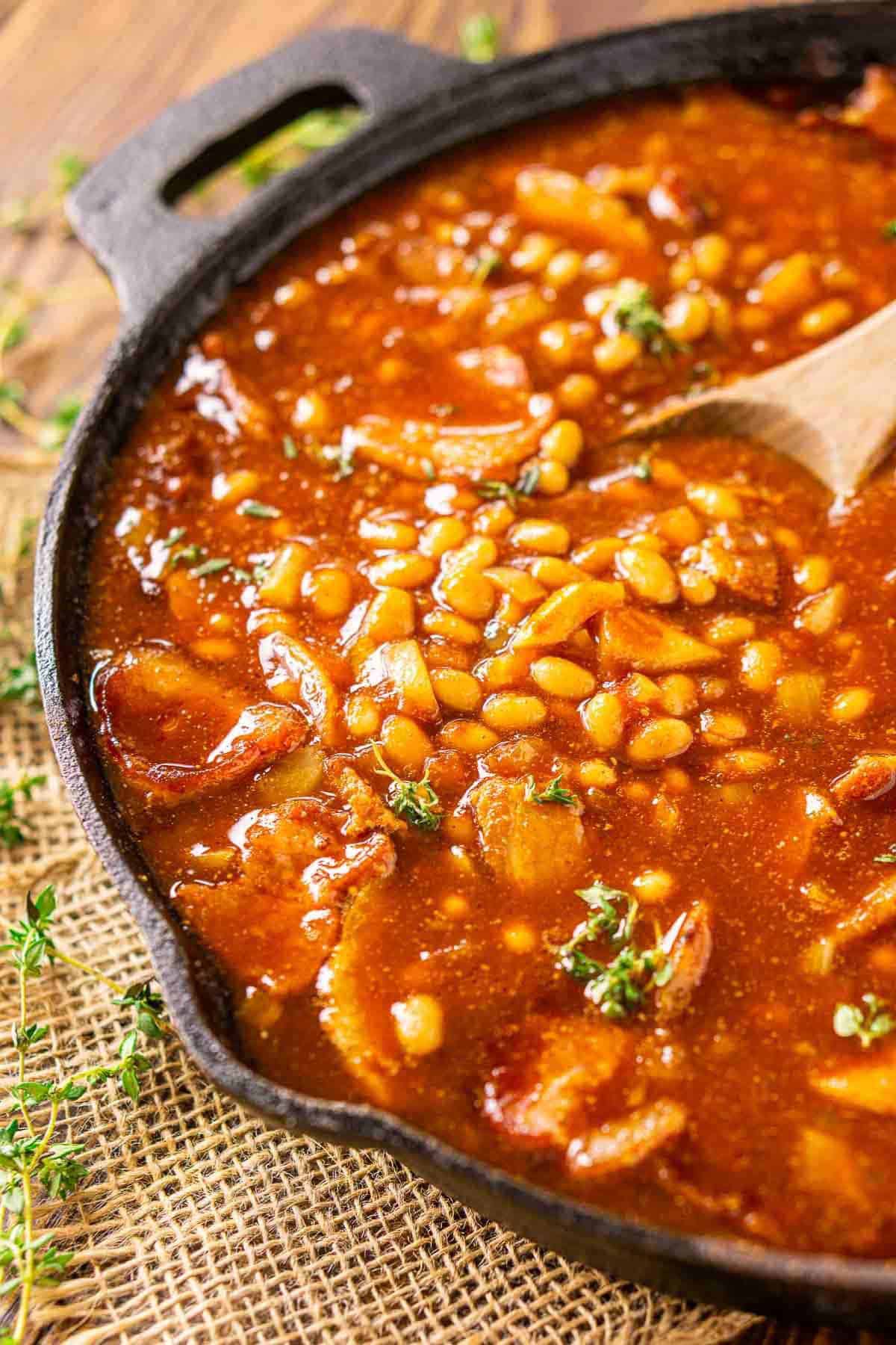 A cast-iron skillet with baked beans on burlap with fresh thyme to the side.