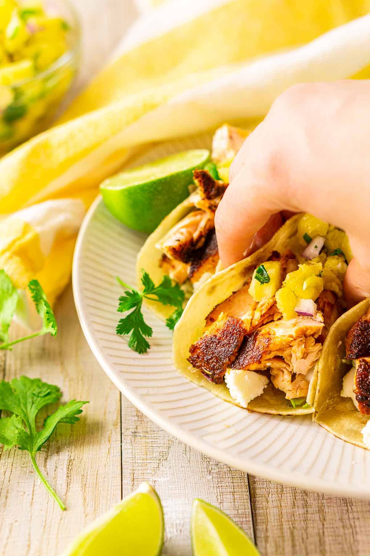 A hand picking up a fish taco from a white plate with cilantro and lime slices around it.