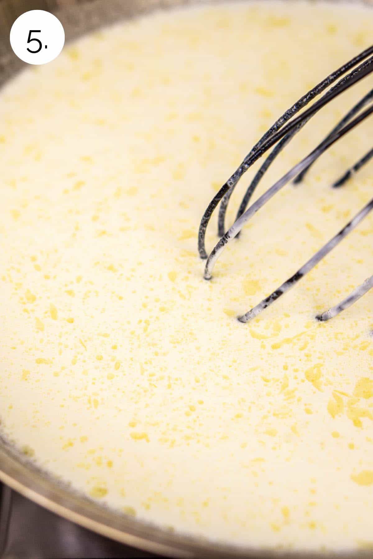 Whisking the heavy cream and milk in a stainless steel skillet on the stove to smooth.