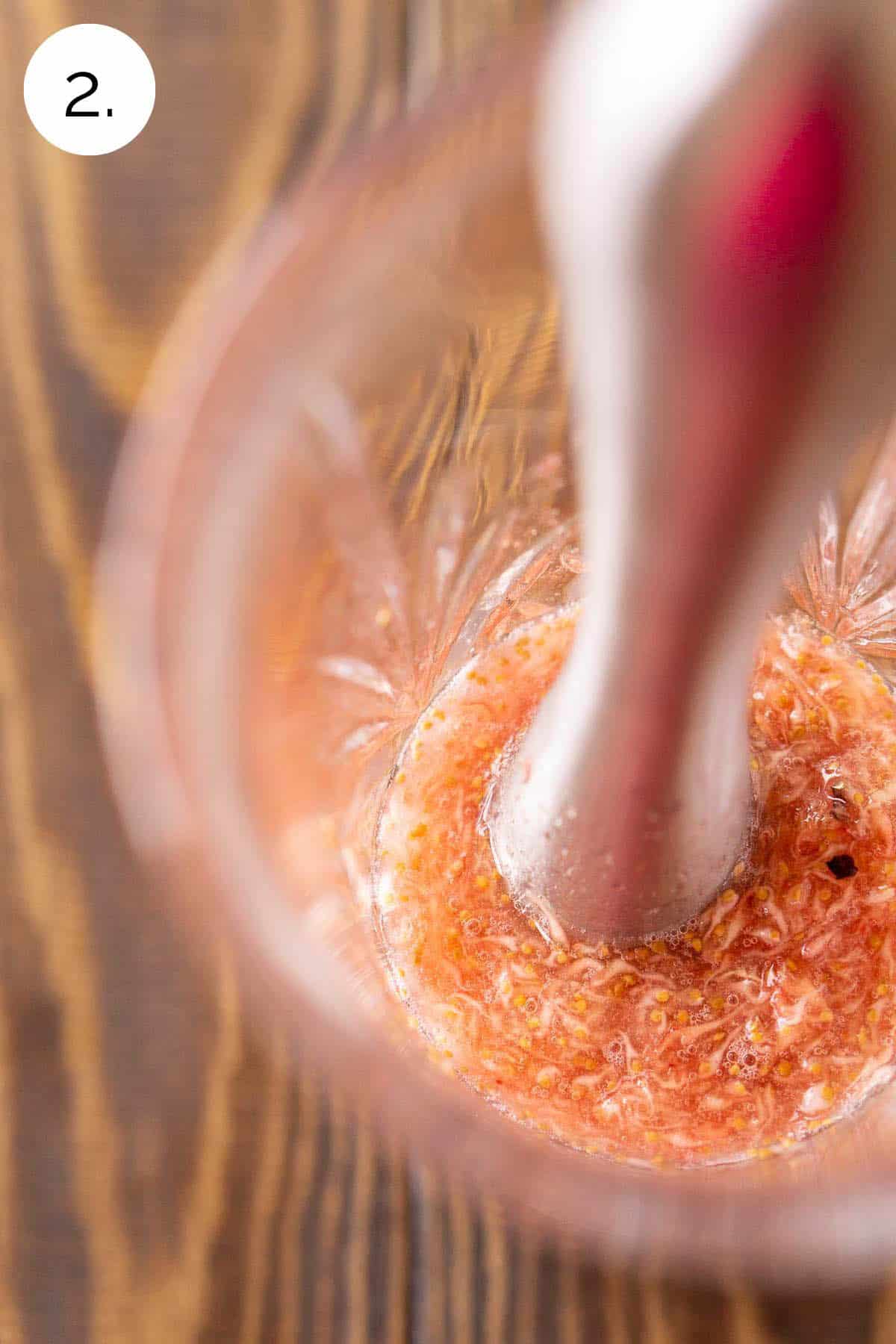 Muddling the fresh figs with the sage simple syrup in a crystal cocktail shaker on a wooden surface.