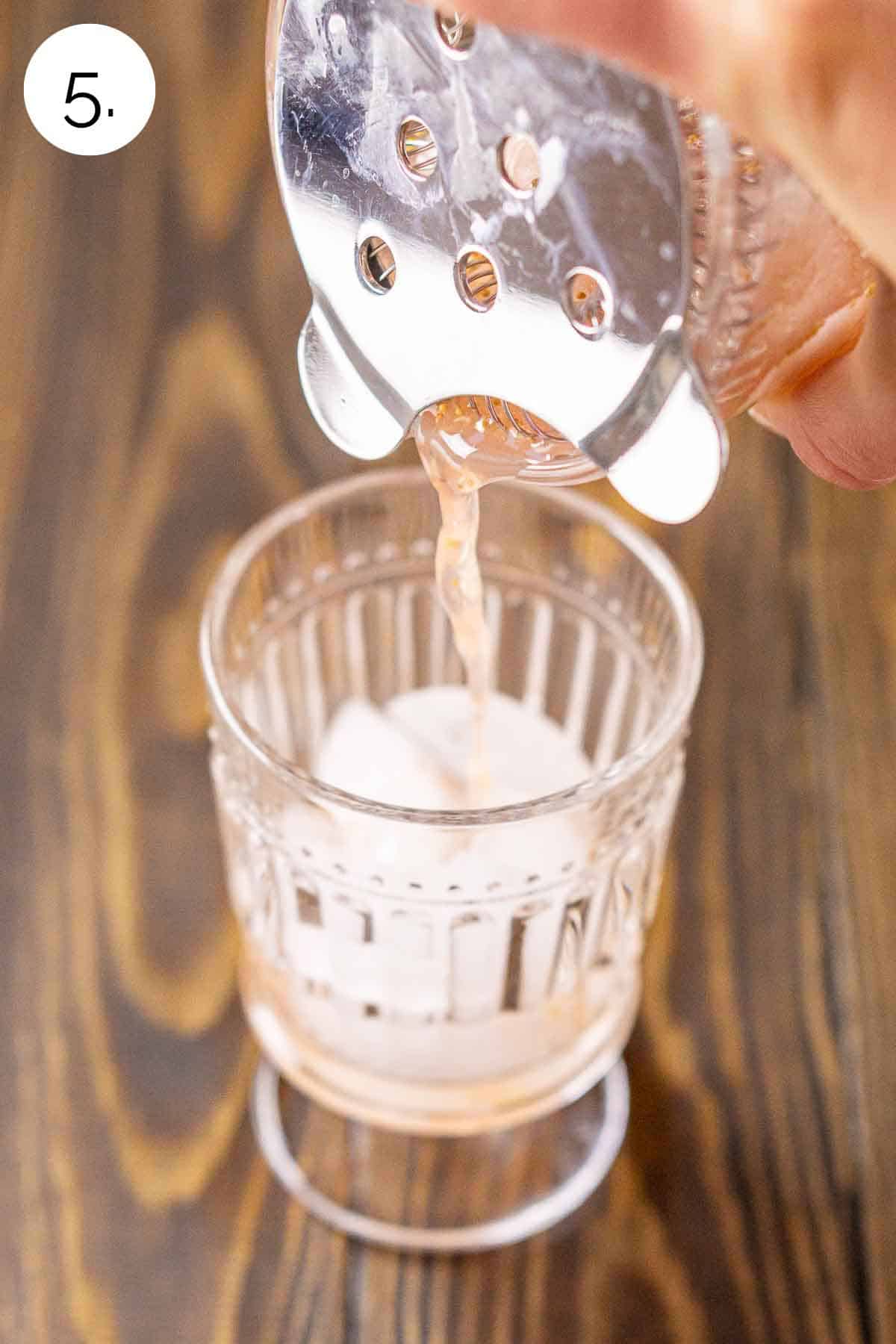 Using a Hawthorne strainer to pour the drink into a glass with ice.