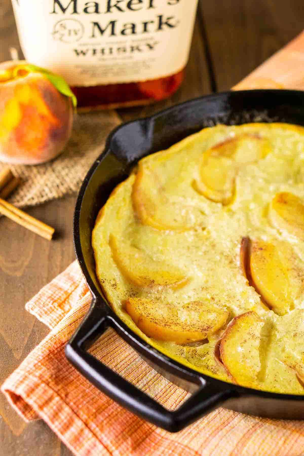 Looking down on a cast-iron skillet filled with the bourbon-peach clafoutis on a summery napkin.
