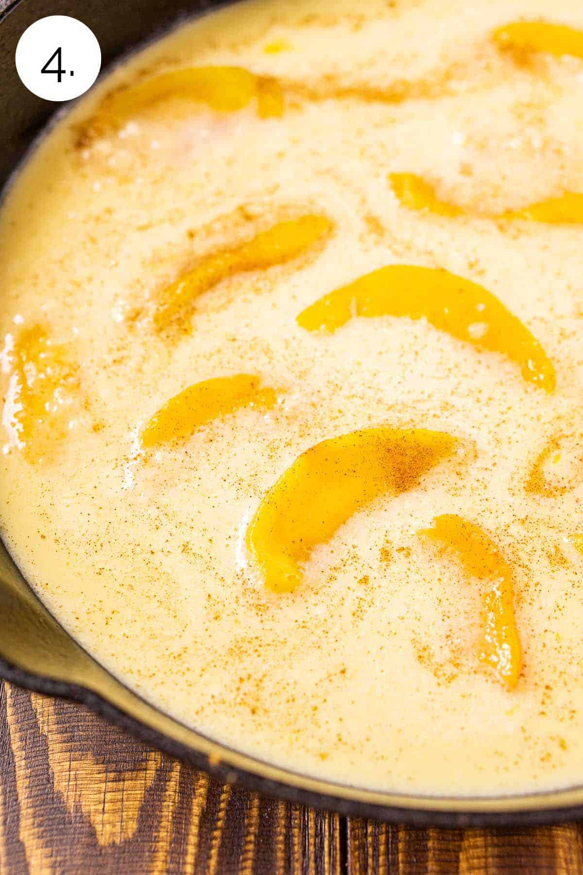 The clafoutis batter in a cast-iron skillet with peaches on top before baking.