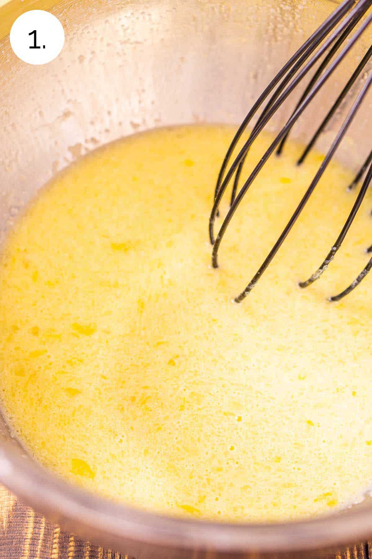 Whisking the wet ingredients together in a stainless steel mixing bowl on a wooden surface.