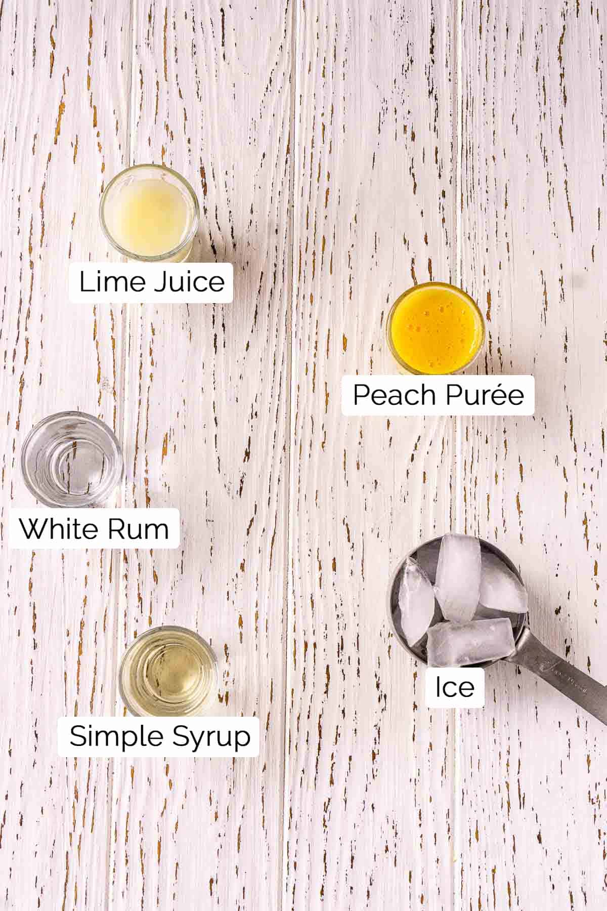 The drink ingredients with black and white labels underneath each item on a white wooden surface.