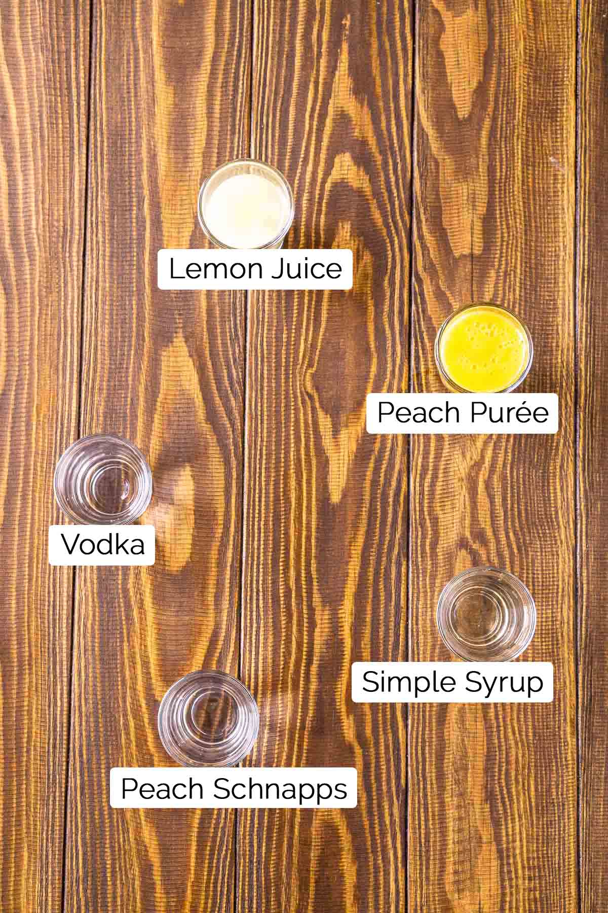 The drink ingredients in shot glasses on a brown wooden surface with black and white labels.