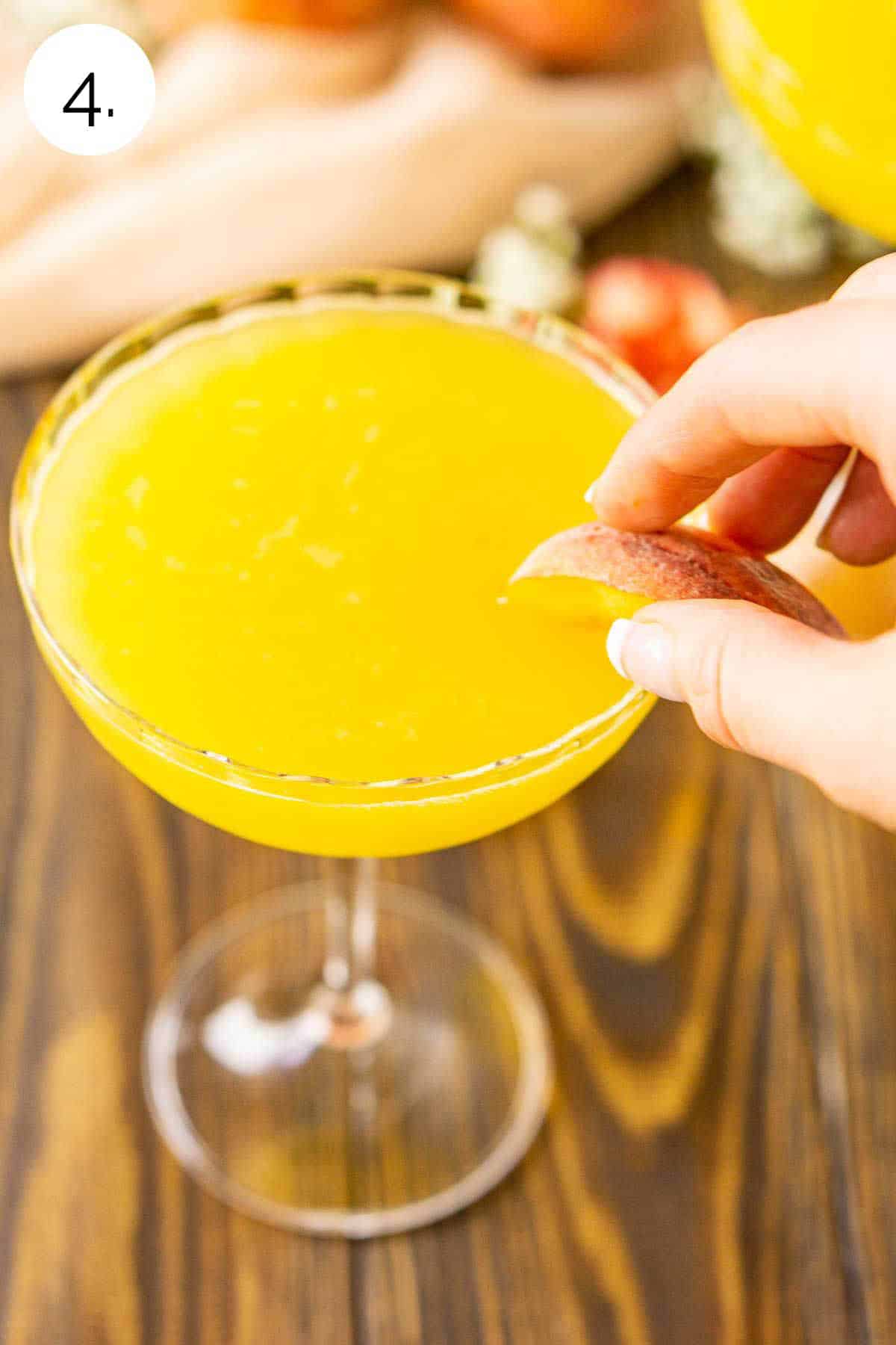 A hand putting the fresh peach slice on the glass to garnish.
