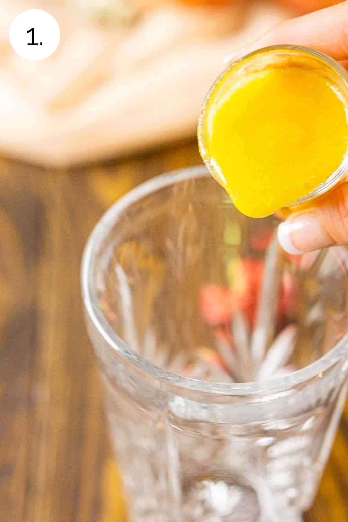 Pouring the peach purée from a shot glass into a crystal cocktail shaker.