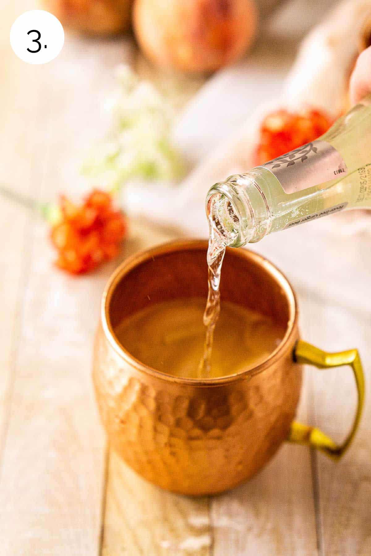 Pouring a bottle of ginger beer into the copper mug on a cream-colored wooden surface.