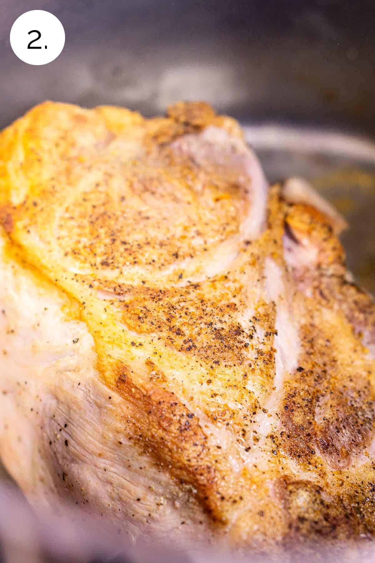 The pork shoulder in a large stainless steel stockpot after it's cooked to form a brown crust.