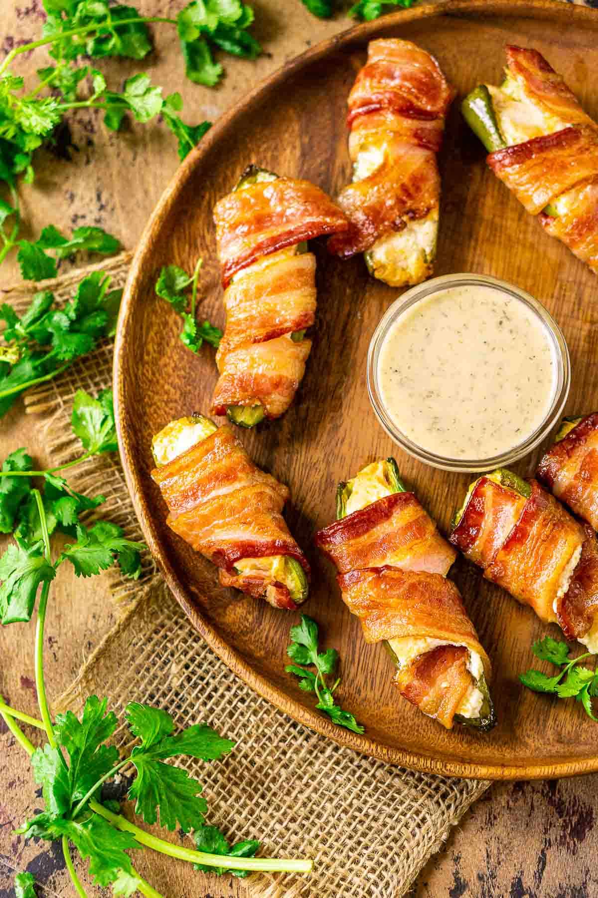 An aerial view of the smoked jalapeño poppers on a wooden plate with fresh cilantro sprigs to the left.