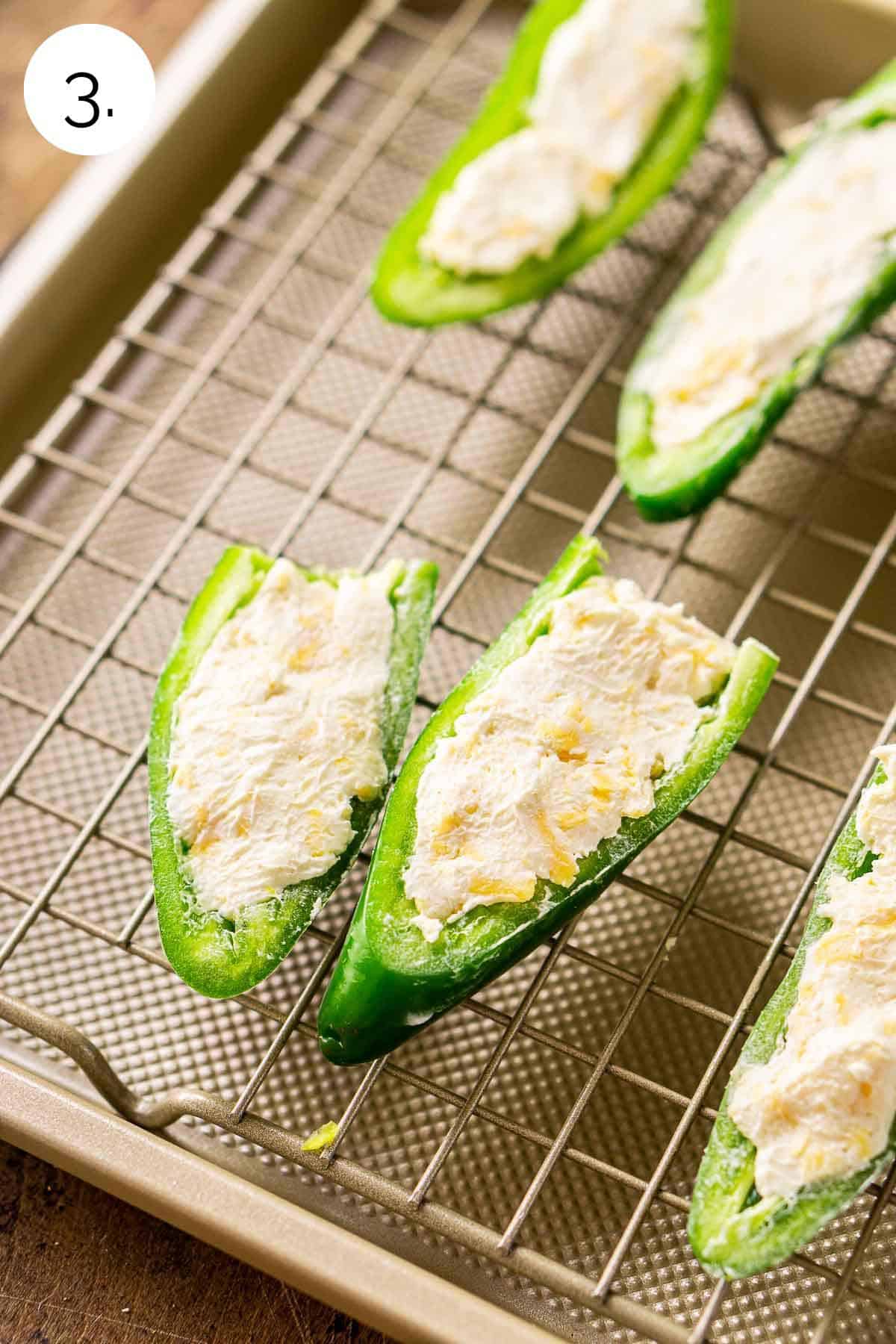 The jalapeño halves filled with the cream cheese mixture on a wire rack on top of a baking sheet.