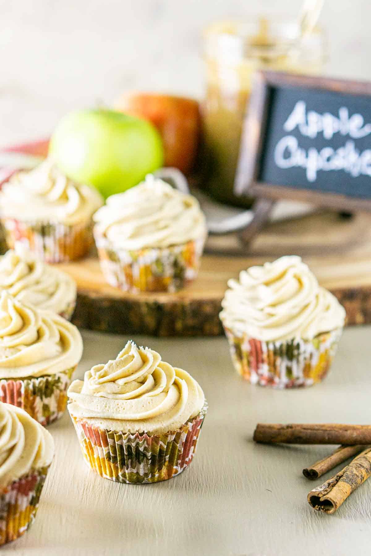 A close-up of an apple spice cupcakes with cinnamon sticks to the right and more cupcakes to the left.