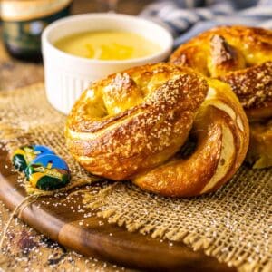 The soft beer pretzels on a wooden tray with burlap and an Oktoberfest beer and cheese sauce in the background.