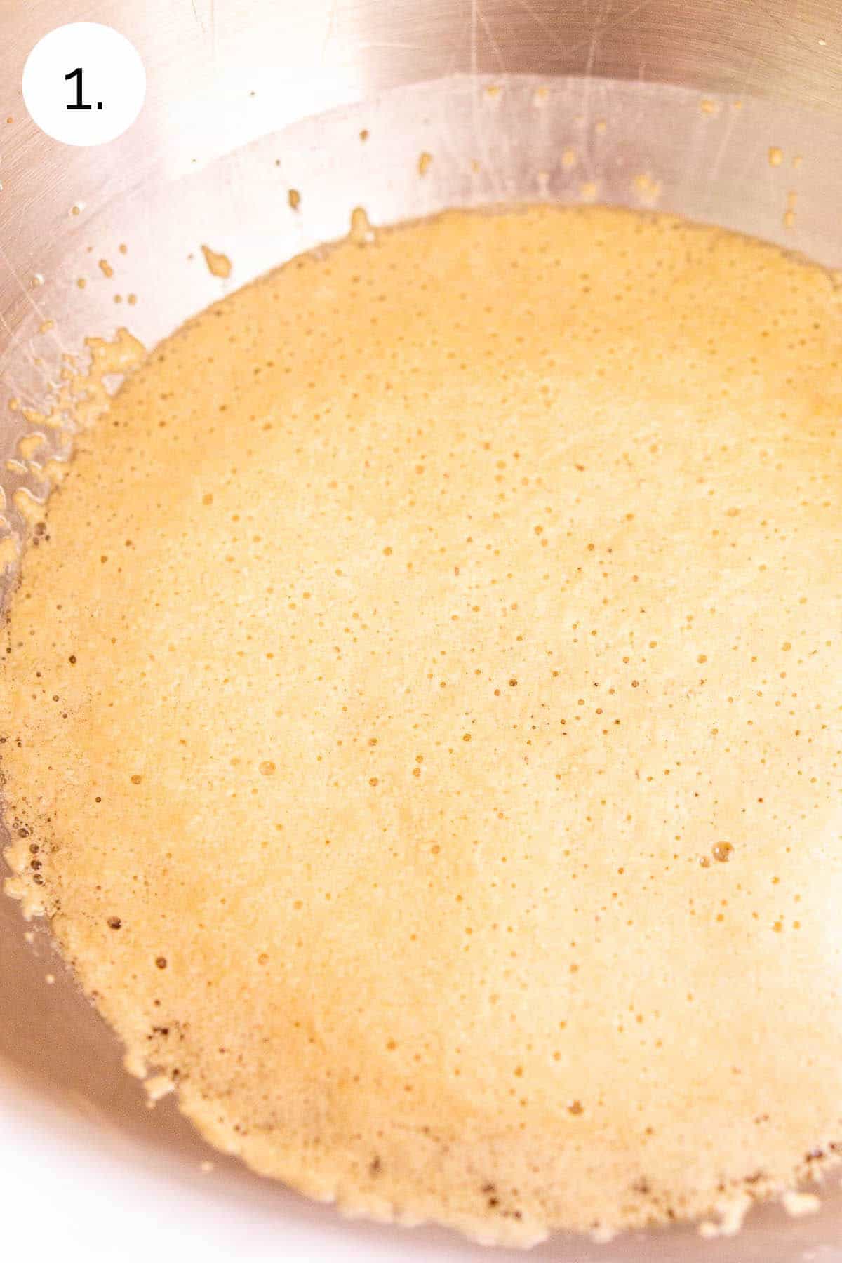 The yeast mixture in a stainless steel mixing bowl after it has turned foamy.