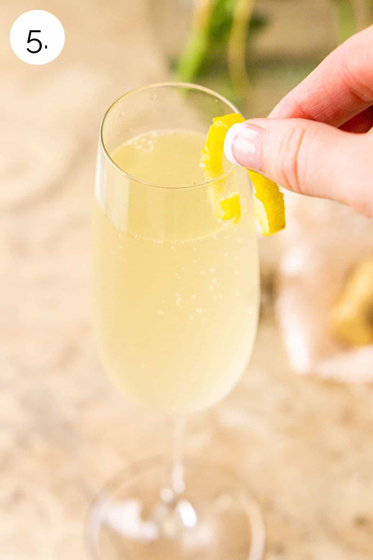 A hand placing the lemon twist on the side of the Champagne flute.