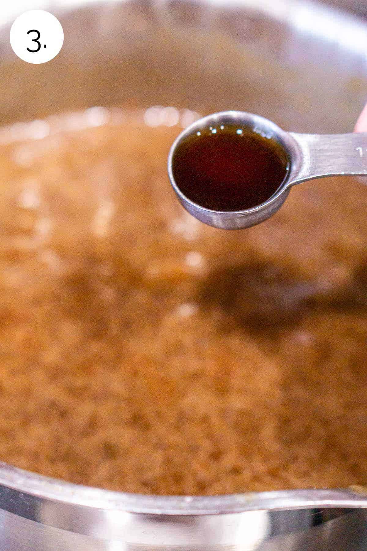 A teaspoon pouring the vanilla extract into the sauce after it had boiled and thickened.