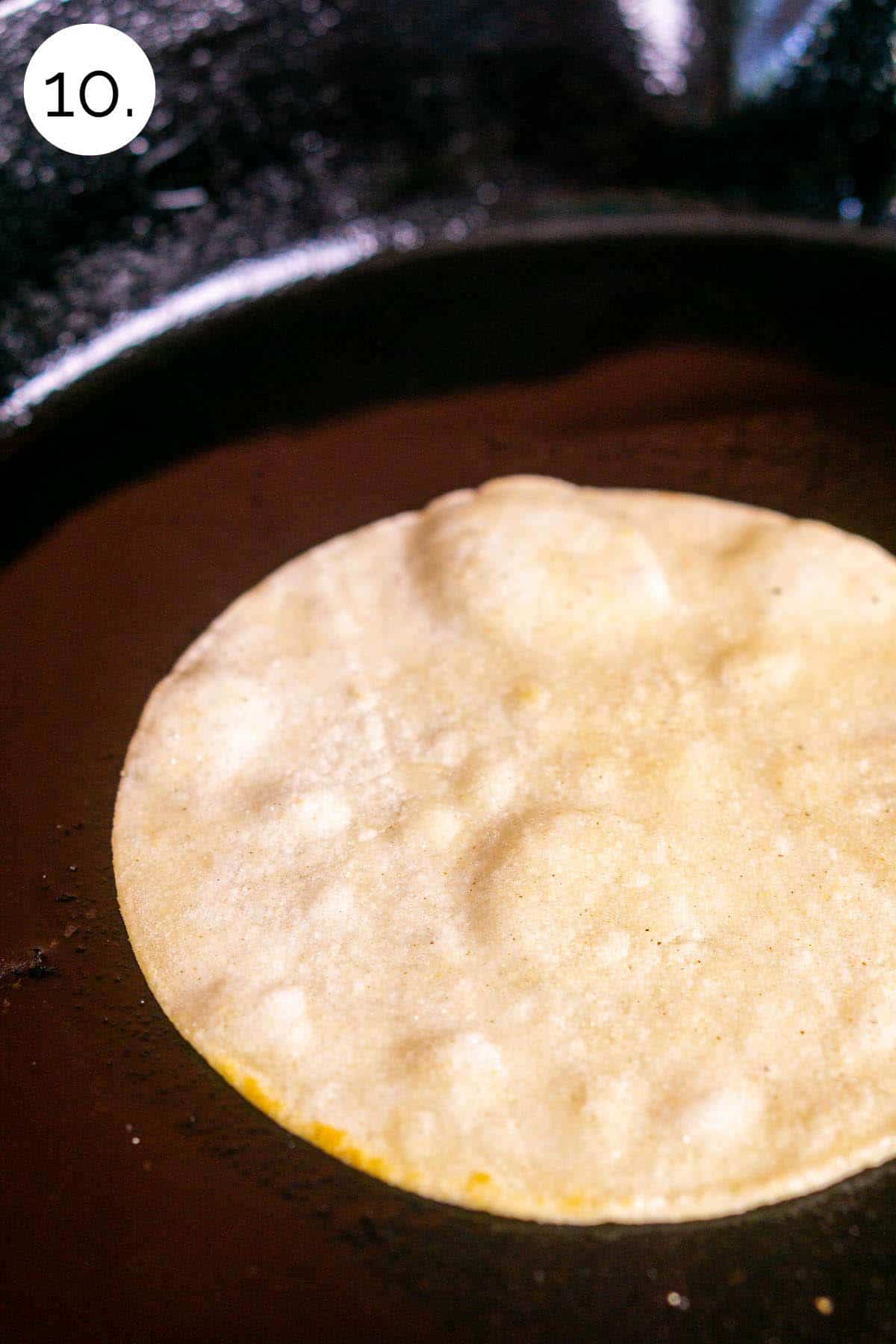 A corn tortillas frying in oil in a cast-iron skillet to make pliable and toast the flavor.