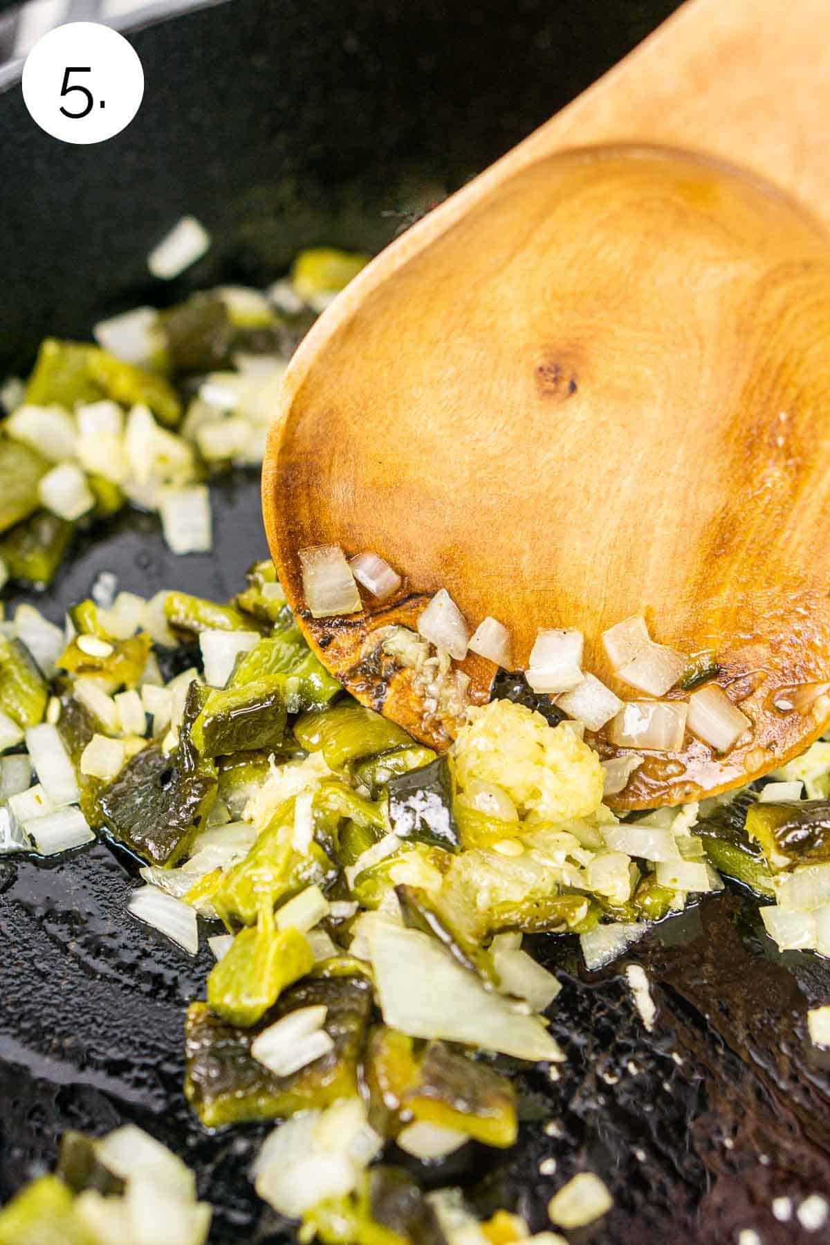 Stirring the peppers, onion and garlic with a wooden spoon in a black cast-iron skillet.