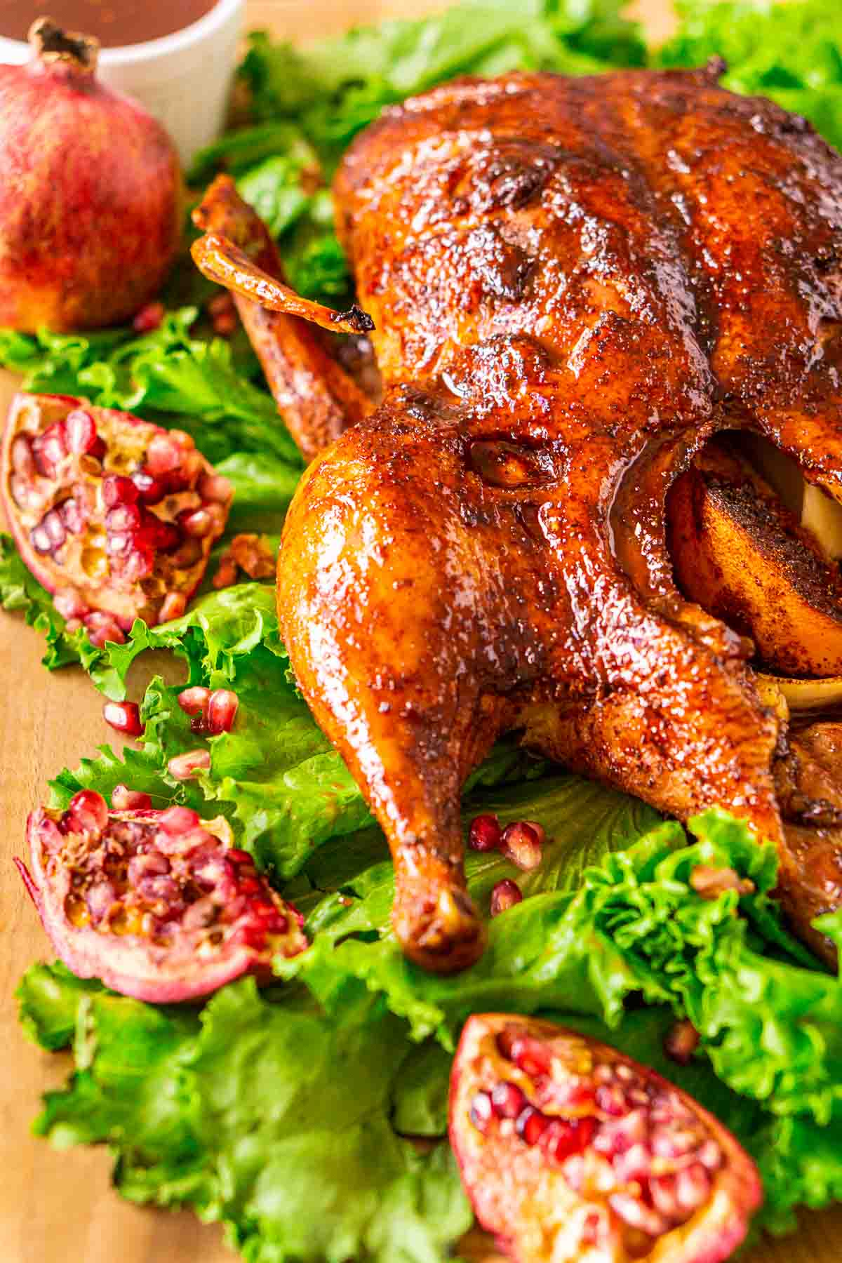 Looking at the smoked duck from the left on a bed of lettuce with pieces of pomegranate to the side.