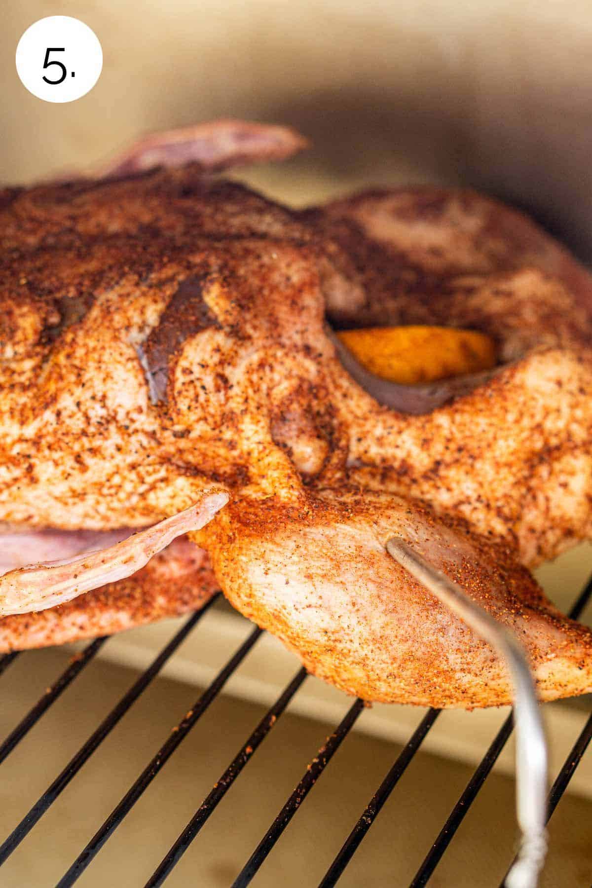 The bird on the grill grates ready to smoke with a probe thermometer stuck in the thigh.