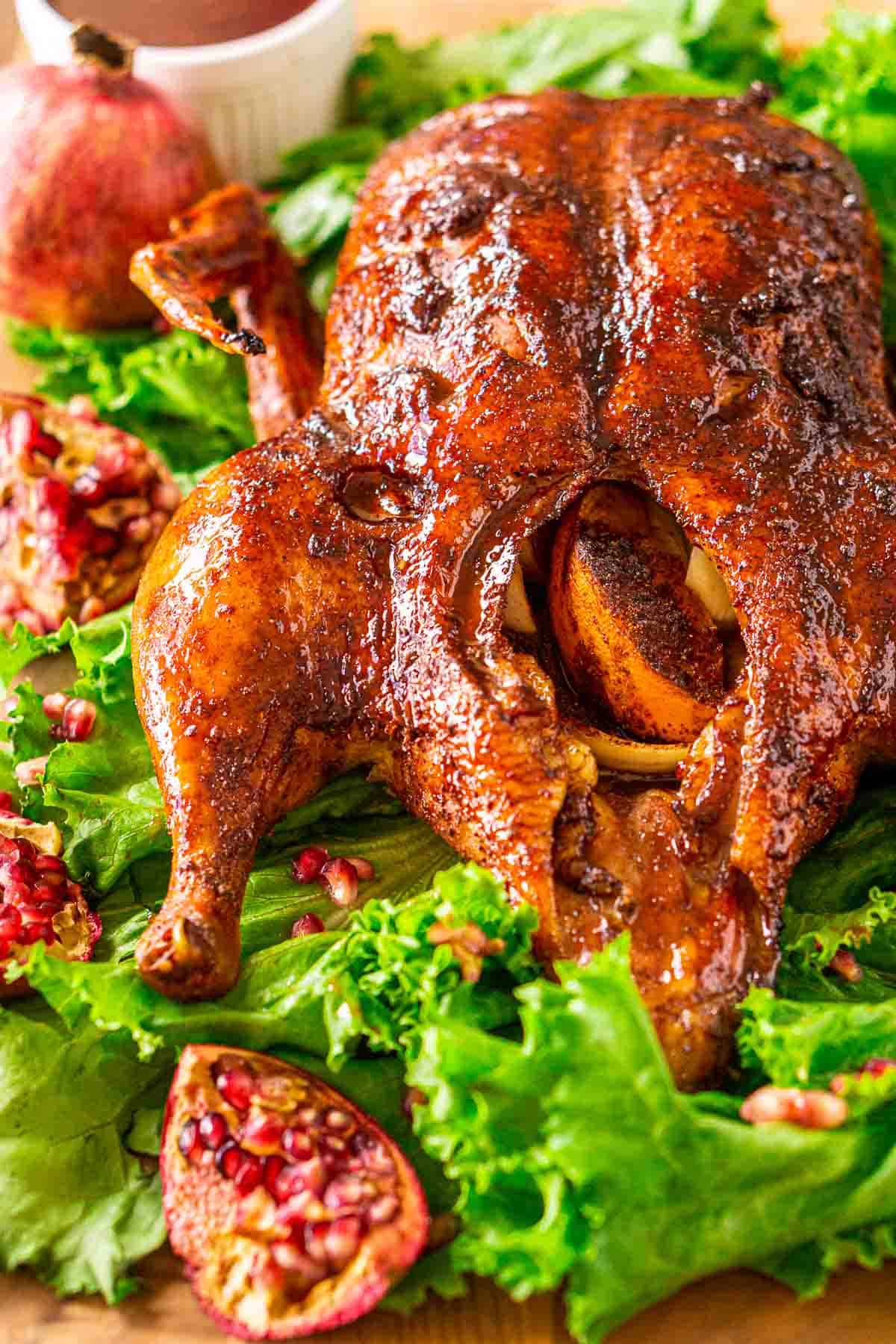 Looking down on the smoked duck on a bed of green lettuce with pomegranates and the glaze to the side.