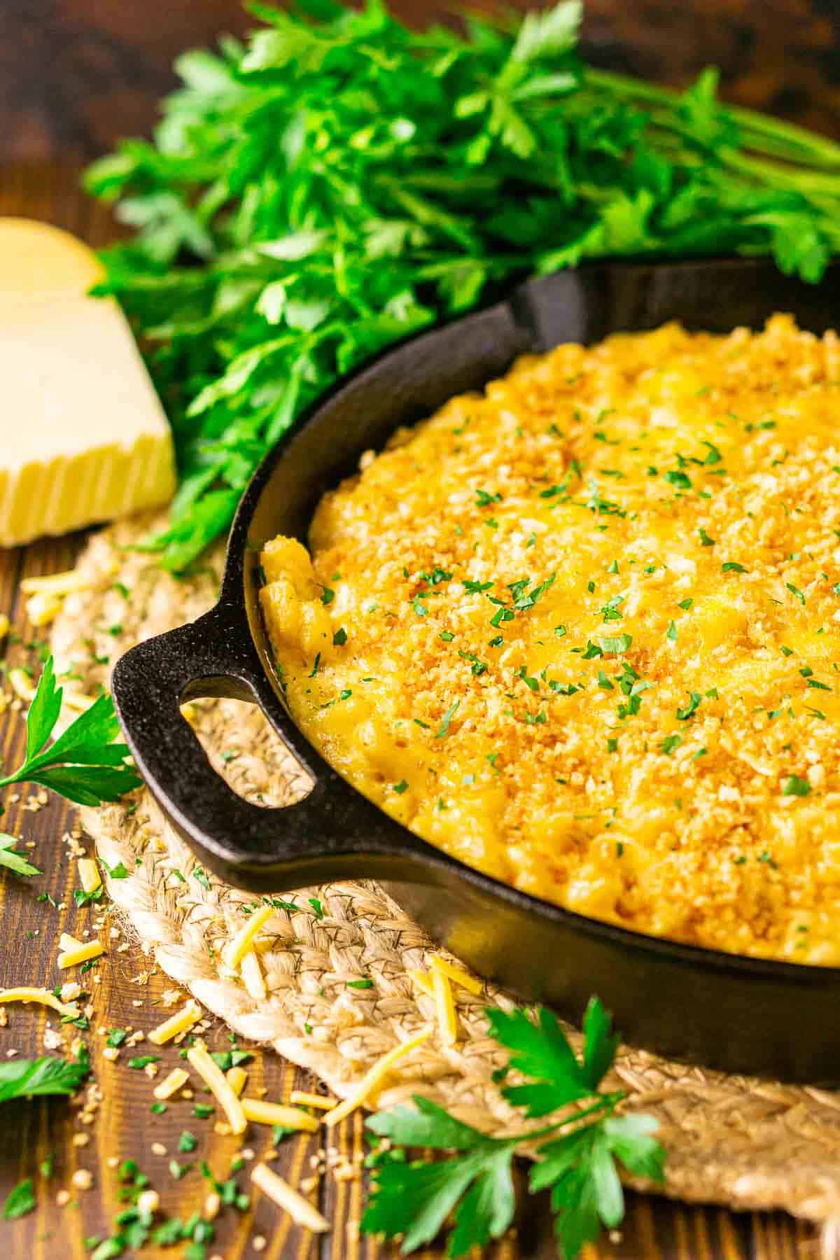 A cast-iron skillet fill with smoked mac and cheese with fresh parsley and shredded cheese around it.