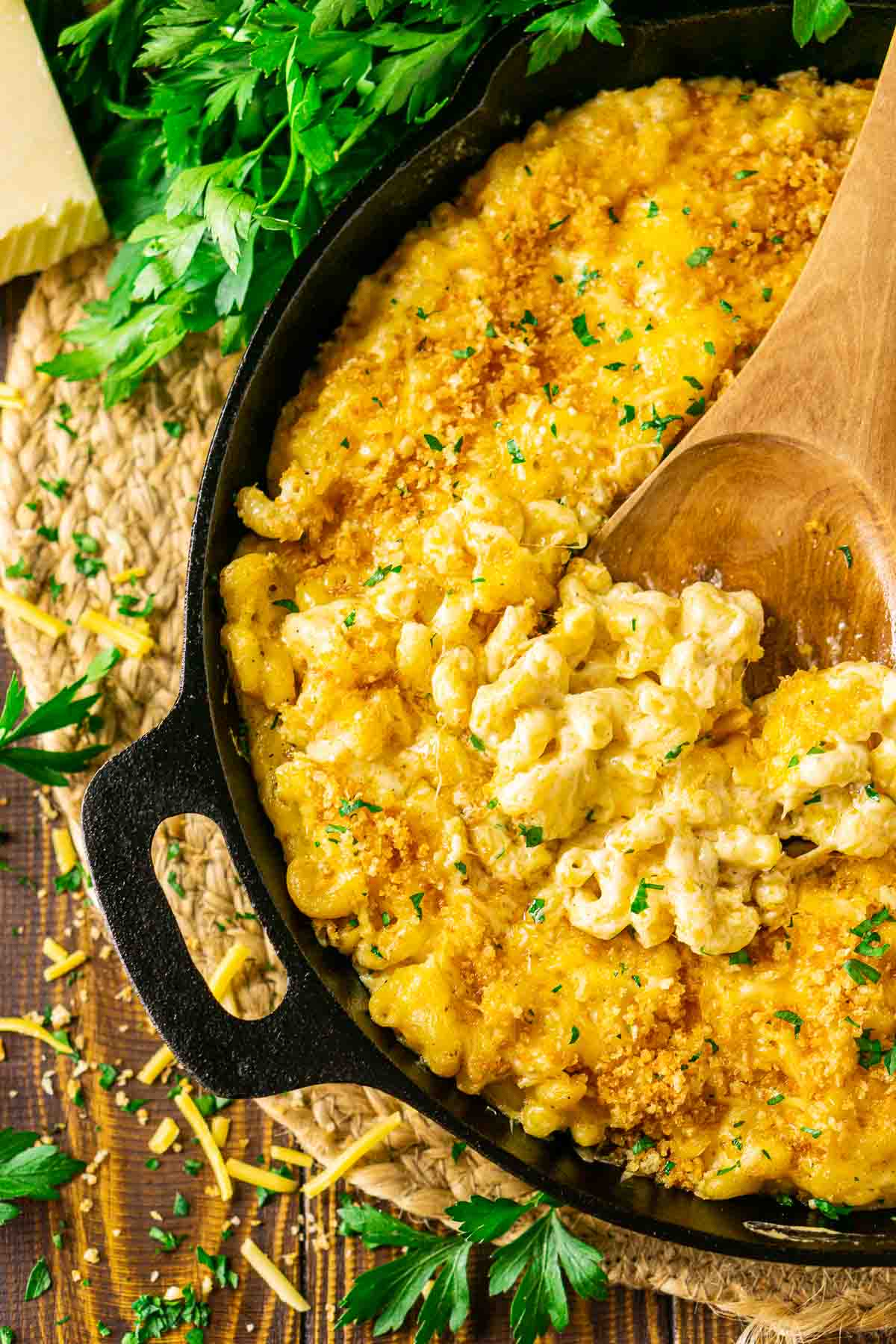 An aerial view of a wooden spoon in the cast-iron skillet with a scoop of the smoked mac and cheese.