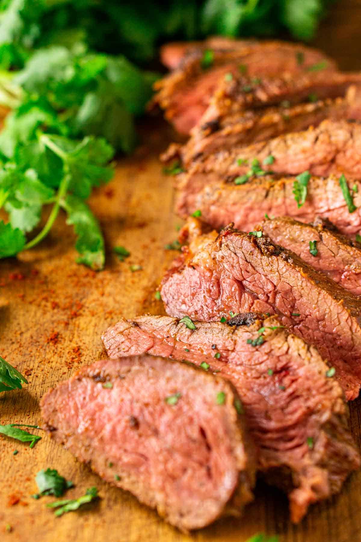 A close-up shot of the tri tip cut into slices on a wooden cutting board with chopped cilantro to the side.