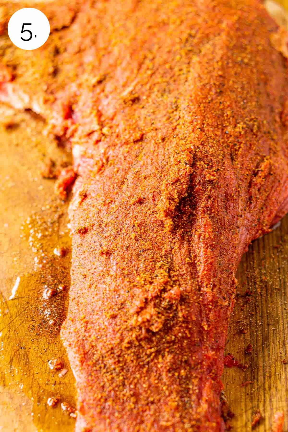 The beef coated in the spice mixture on a wooden cutting board before going on the smoker.