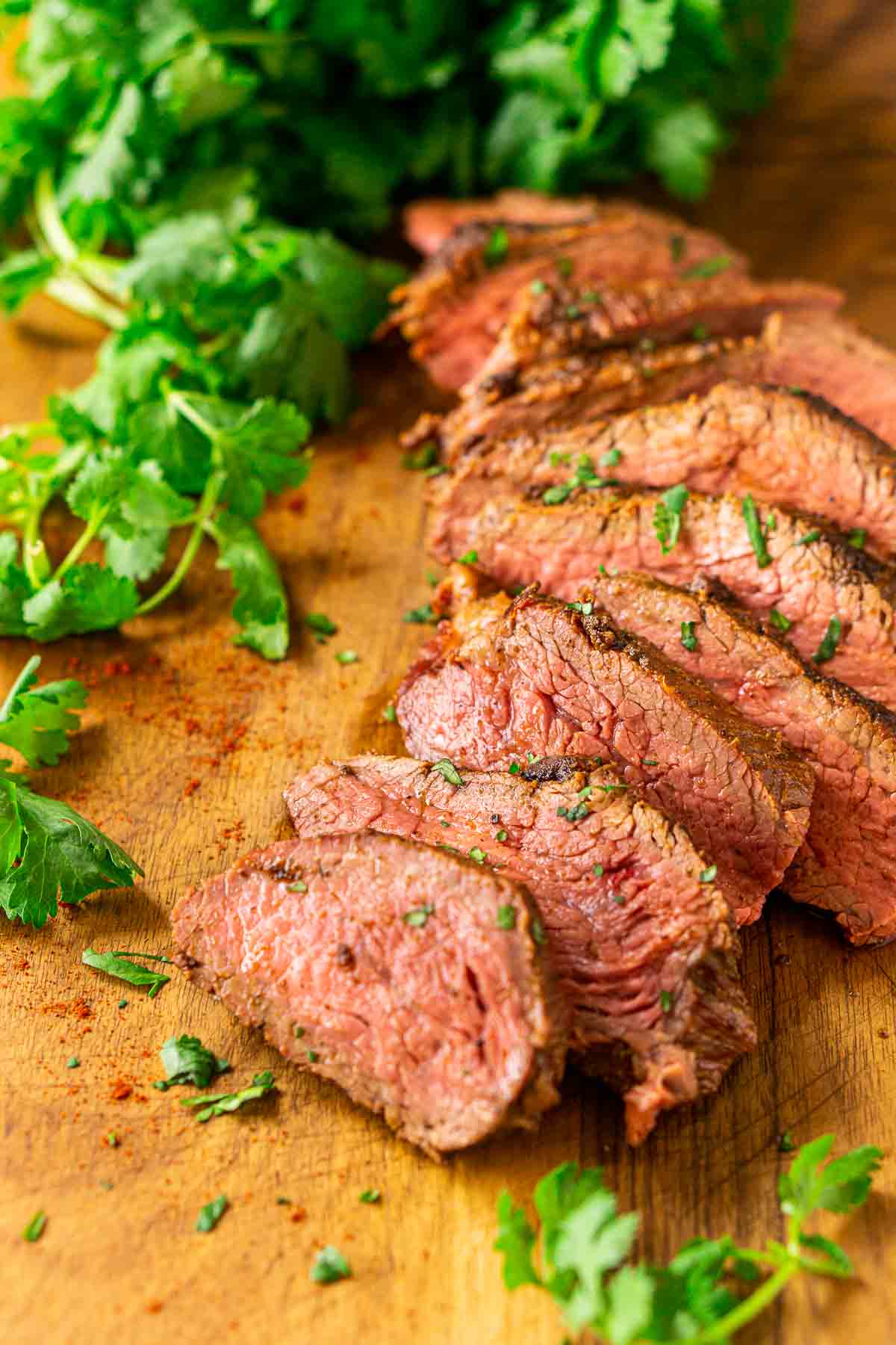 The smoked tri tip on a wooden cutting board with fresh cilantro surrounding it and the spice mixture sprinkled around it.