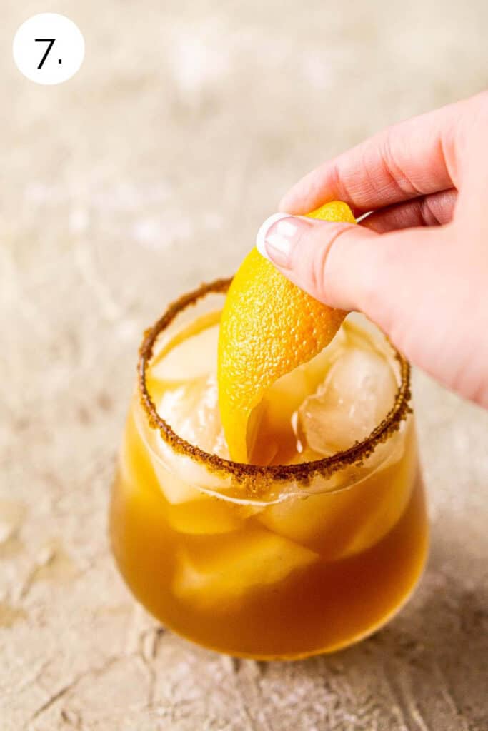 A hand dropping the orange twist into the drink as a garnish.