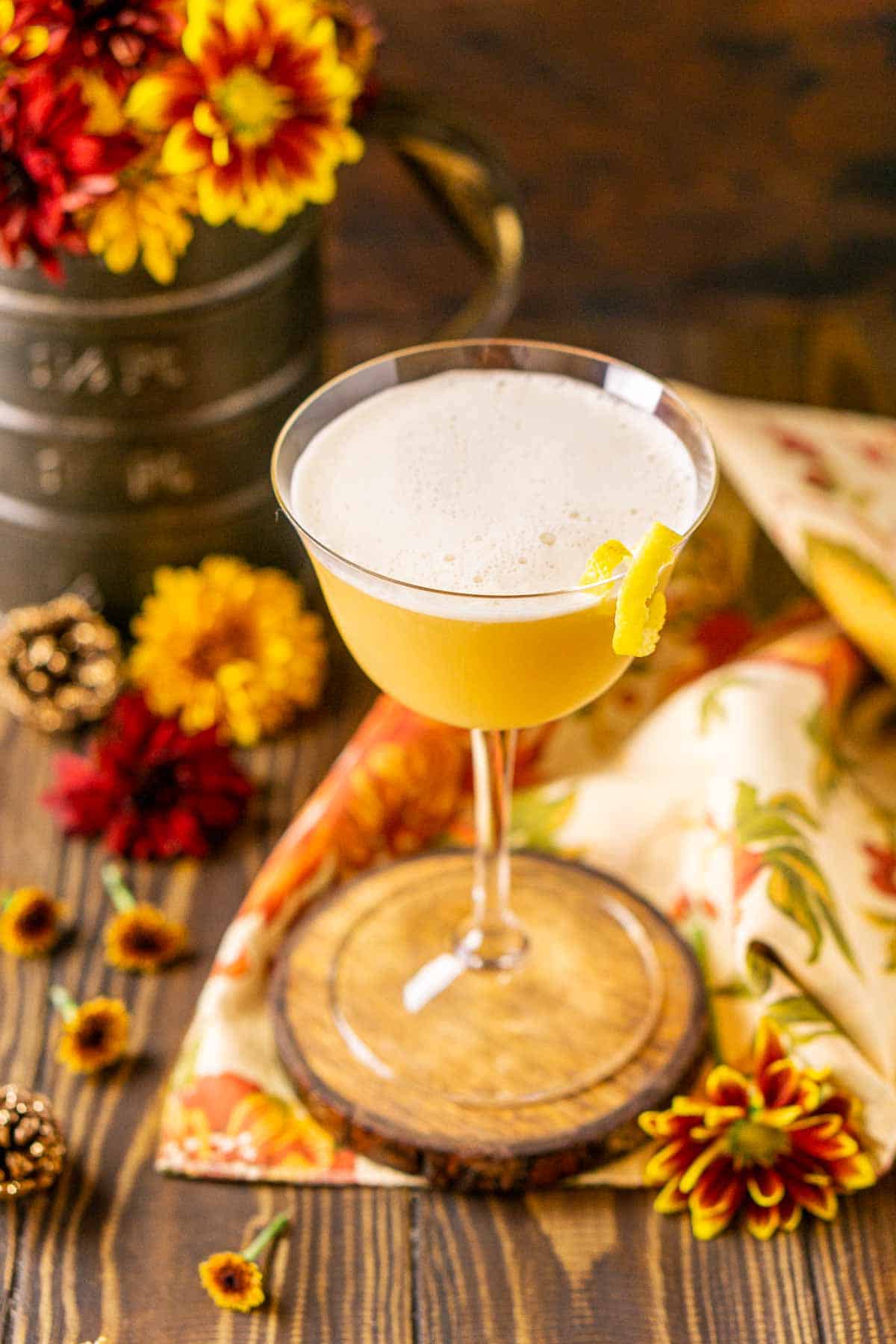 Looking down on the frothy topping of the maple whiskey sour with fall flowers scattered around it.