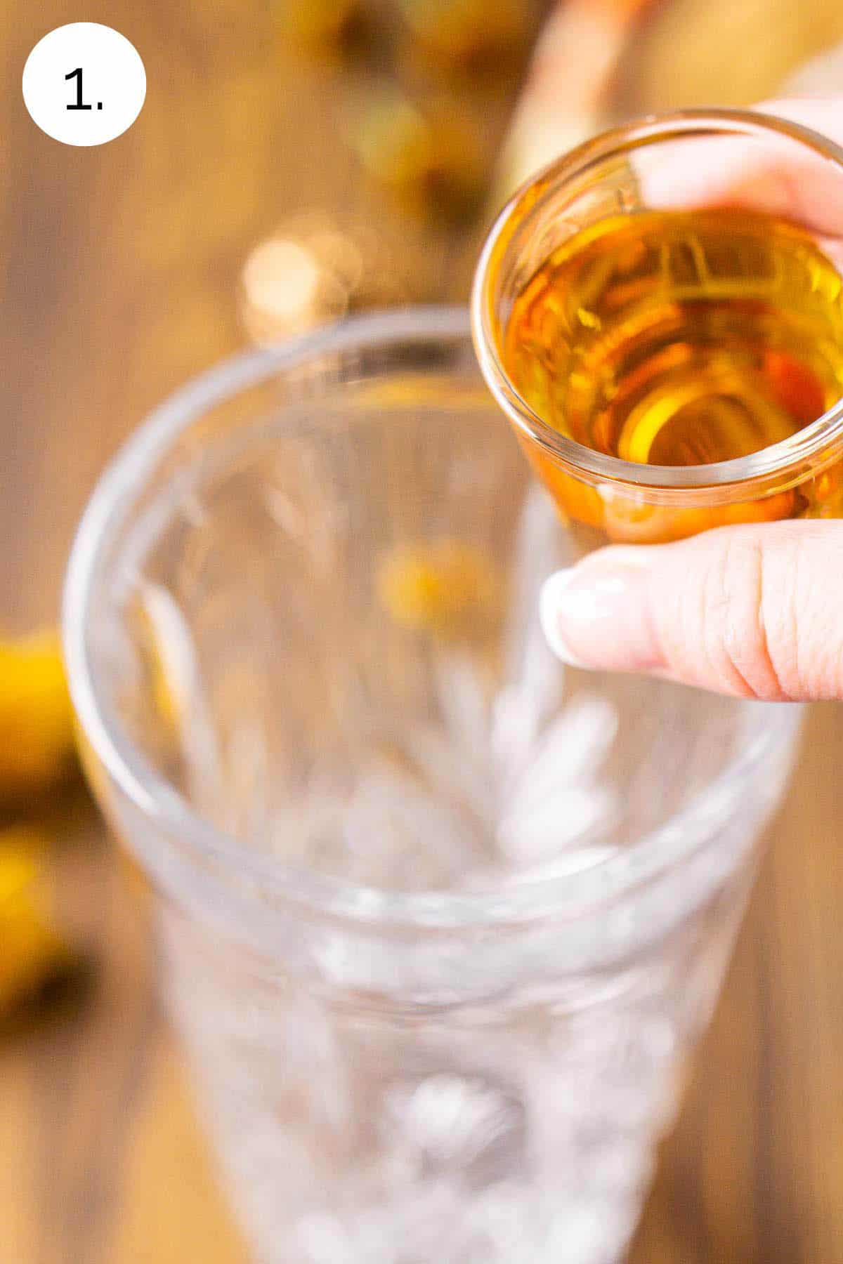 A hand holding a shot of bourbon over the cocktail shaker to pour it in the glass.