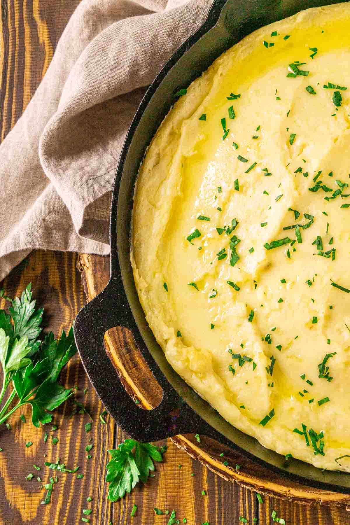 An aerial view of the smoked mashed potatoes on a wooden surface with chopped parsley to the side.