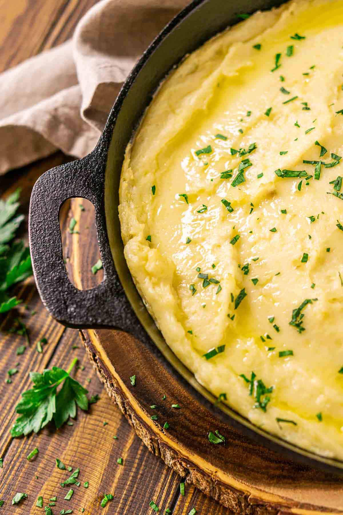 A side view of the cast-iron skillet filled with the smoked mashed potatoes on a wooden platter.