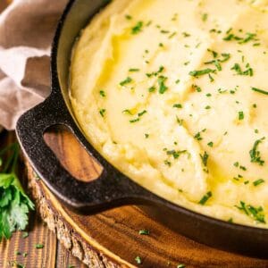 A black cast-iron skillet filled with the smoked mashed potatoes with chopped parsley to the left and a napkin in the background.