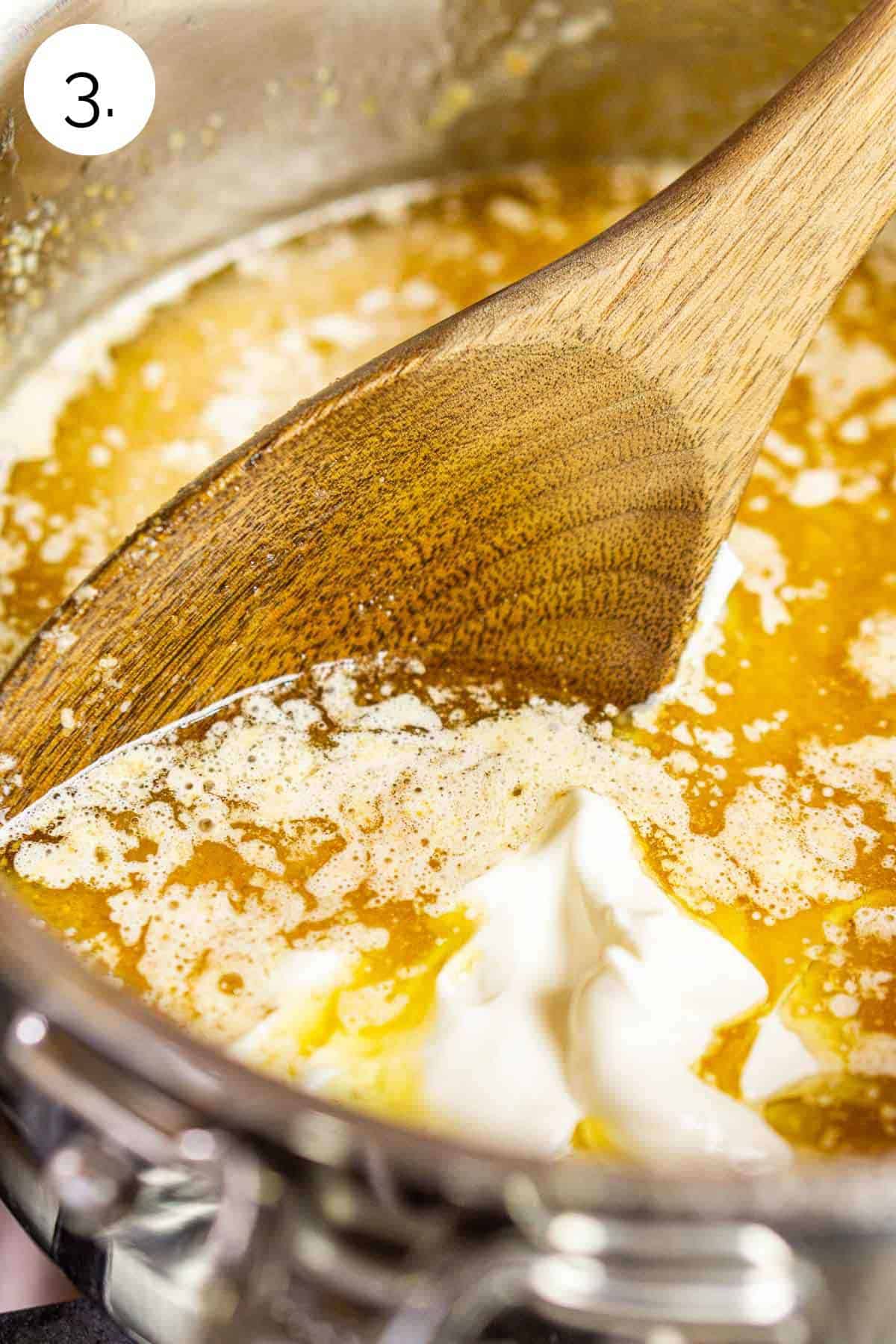Stirring together the brown butter, sour cream and heavy cream in a stainless steel saucepan on the stove-top.