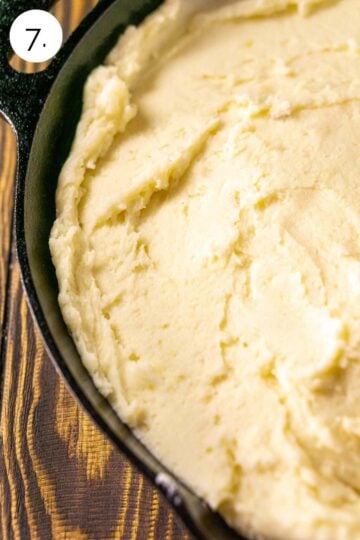 The mashed potatoes spooned into a black cast-iron skillet on a wooden surface before smoking.